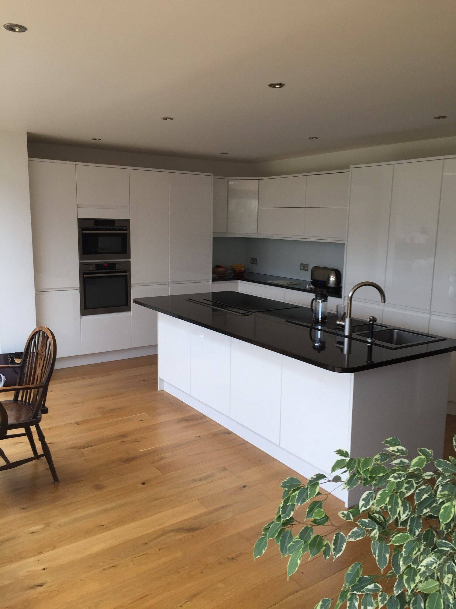 White gloss kitchen with a dark worktop island, built-in double oven and oak floor