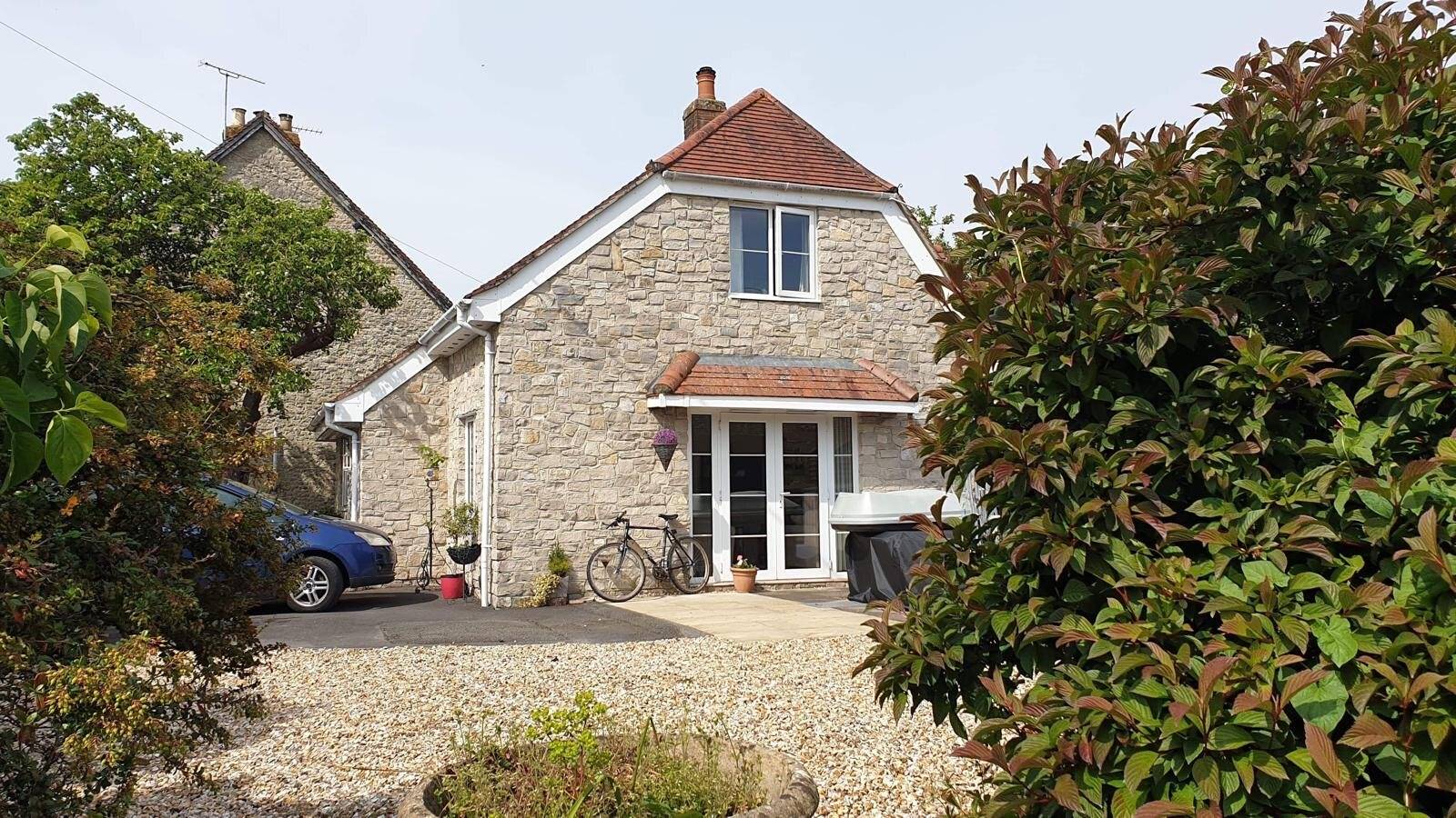 Stone-built cottage with white French doors under a red tiled canopy and a gravel drive